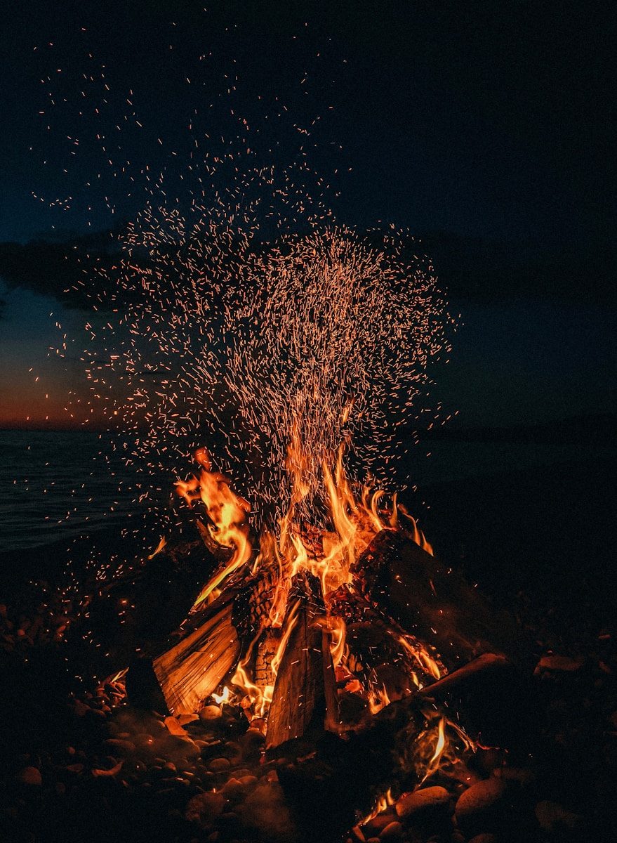 A bright campfire with rising sparks on a dark beach at night